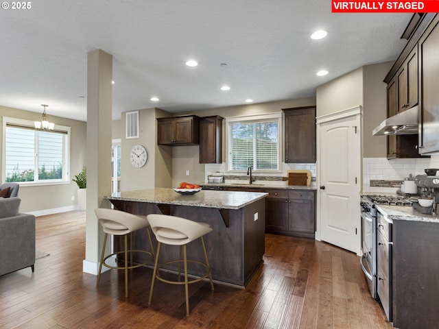 kitchen featuring under cabinet range hood, gas stove, dark brown cabinets, and visible vents