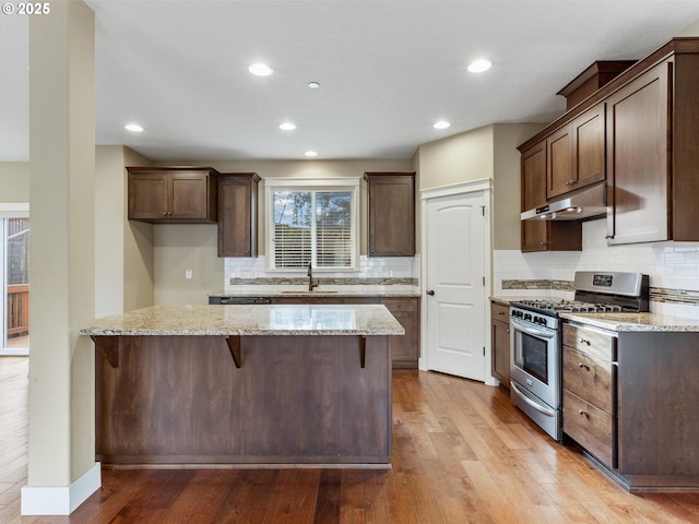 kitchen featuring decorative backsplash, gas range, light stone counters, and under cabinet range hood
