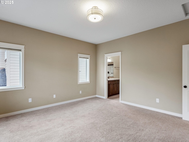 spare room with a sink, light colored carpet, baseboards, and a textured ceiling