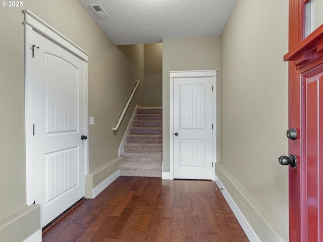 foyer entrance featuring dark wood-type flooring, a textured ceiling, visible vents, stairway, and baseboards