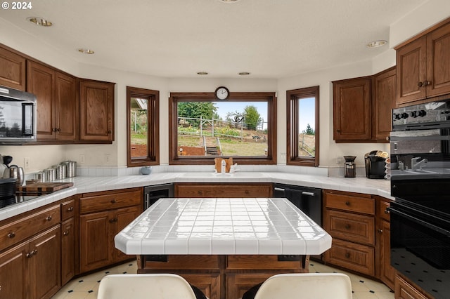 kitchen with black appliances, a kitchen island, sink, and tile countertops