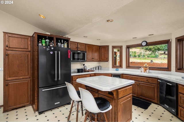 kitchen featuring lofted ceiling, a kitchen island, black appliances, tile countertops, and a breakfast bar area