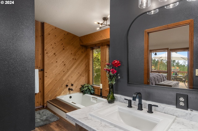 bathroom with wood-type flooring, a textured ceiling, a bathtub, an inviting chandelier, and wooden walls