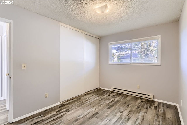 empty room featuring baseboard heating, hardwood / wood-style flooring, and a textured ceiling