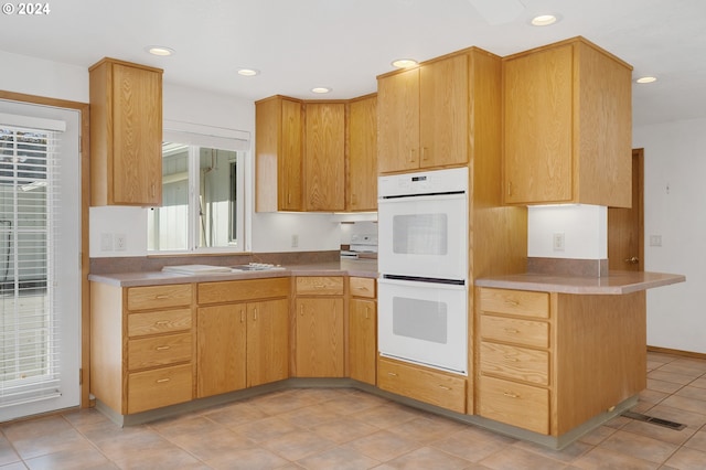 kitchen with a healthy amount of sunlight, kitchen peninsula, white appliances, and light tile patterned floors