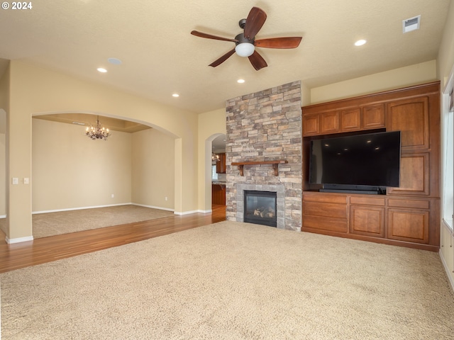 unfurnished living room featuring ceiling fan with notable chandelier, a stone fireplace, wood-type flooring, and a textured ceiling