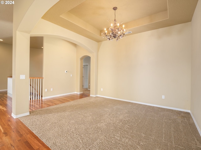 unfurnished room featuring a notable chandelier, hardwood / wood-style floors, and a raised ceiling