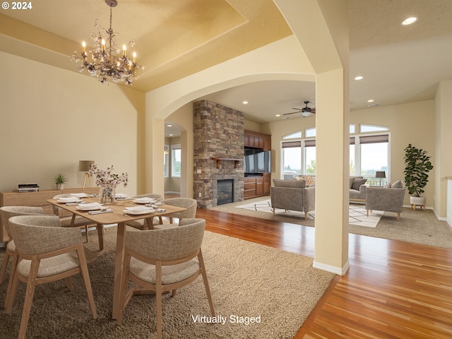 dining space featuring a fireplace, ceiling fan with notable chandelier, light hardwood / wood-style flooring, and a textured ceiling