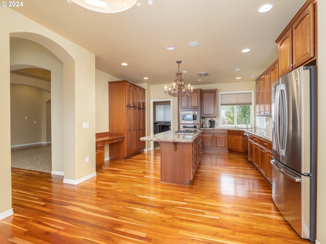 kitchen with light hardwood / wood-style floors, a kitchen island, light stone countertops, hanging light fixtures, and appliances with stainless steel finishes