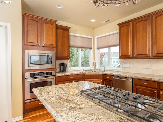 kitchen featuring light stone countertops, decorative backsplash, stainless steel appliances, sink, and light hardwood / wood-style flooring