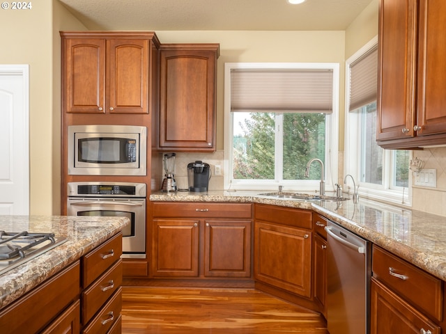 kitchen featuring light wood-type flooring, light stone countertops, tasteful backsplash, sink, and appliances with stainless steel finishes