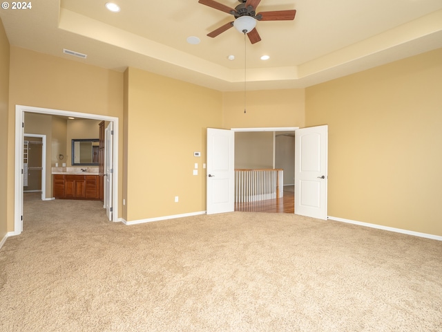 unfurnished bedroom with ceiling fan, light colored carpet, a tray ceiling, and connected bathroom