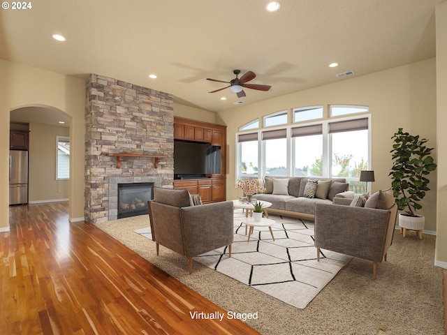 living room featuring hardwood / wood-style flooring, ceiling fan, and a stone fireplace