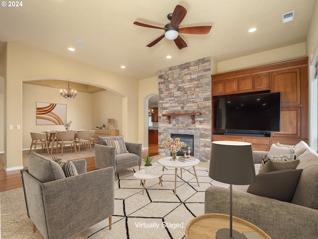 living room featuring ceiling fan with notable chandelier, a stone fireplace, and light hardwood / wood-style flooring