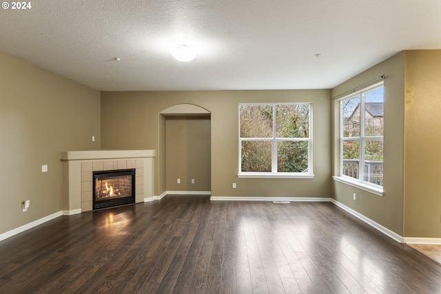 unfurnished living room featuring a tiled fireplace, dark hardwood / wood-style flooring, and a textured ceiling