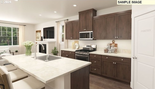 kitchen with dark brown cabinetry, sink, stainless steel appliances, a breakfast bar area, and a center island with sink