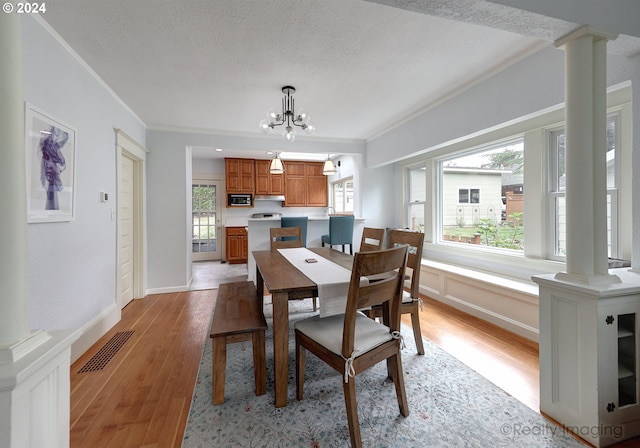 dining area with a textured ceiling, decorative columns, crown molding, and light hardwood / wood-style flooring