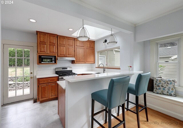 kitchen featuring ornamental molding, sink, hanging light fixtures, appliances with stainless steel finishes, and a kitchen bar