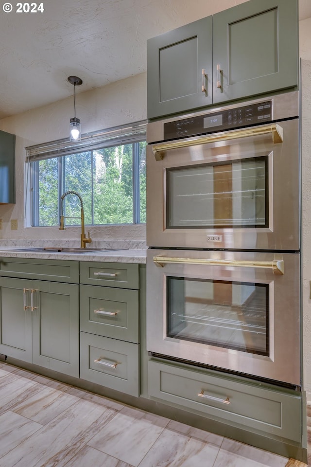 kitchen featuring hanging light fixtures, green cabinetry, a sink, and stainless steel double oven