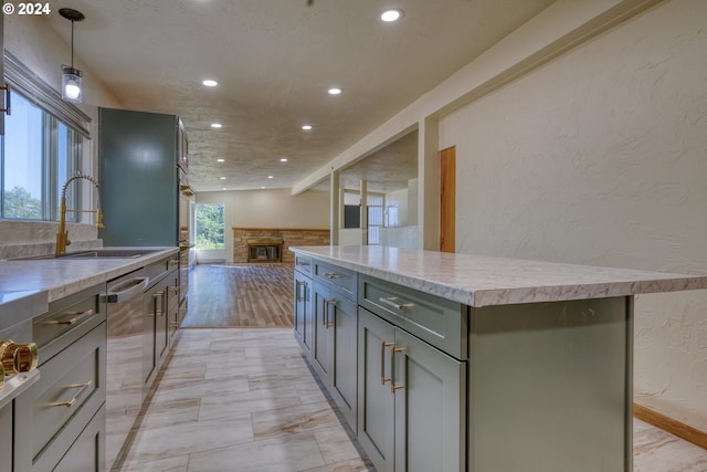 kitchen with a sink, a kitchen island, dishwasher, a stone fireplace, and a textured wall