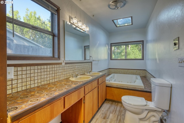 bathroom with toilet, a jetted tub, vanity, backsplash, and wood finished floors