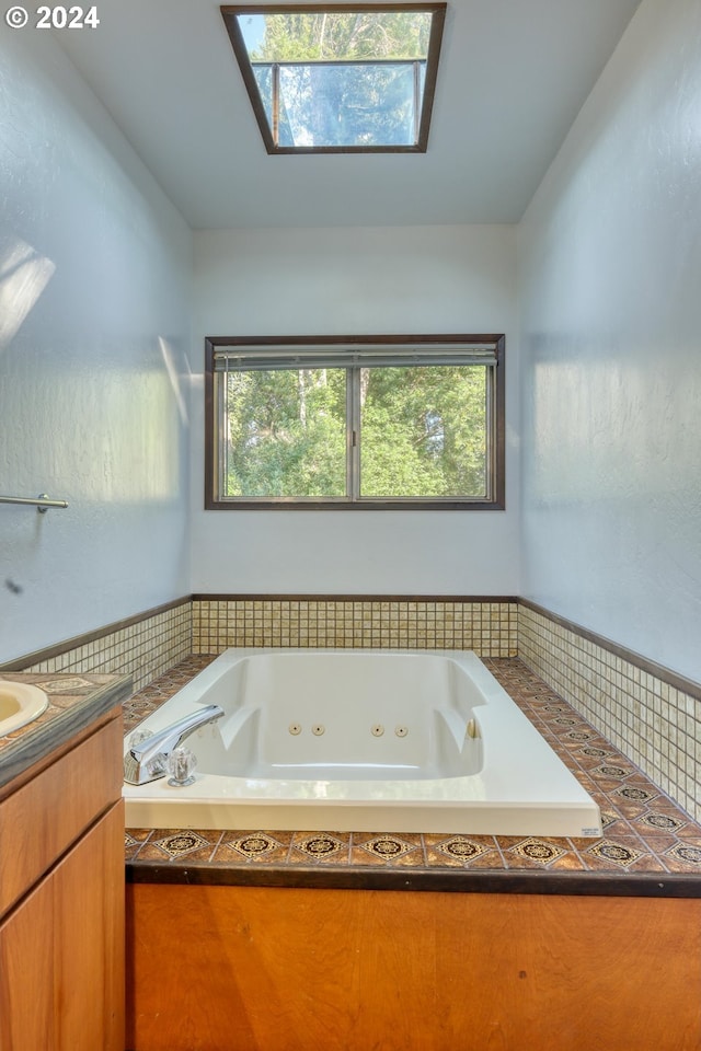 bathroom with tiled tub, a skylight, and vanity