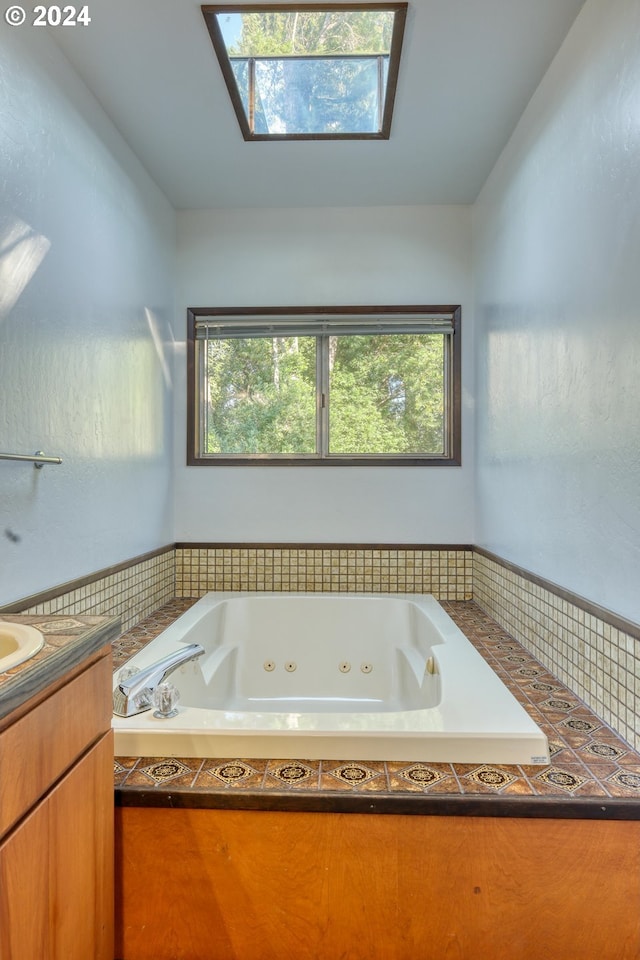 full bathroom featuring vaulted ceiling with skylight, a jetted tub, and vanity