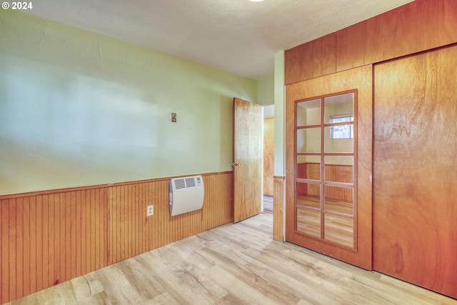 empty room with light wood-type flooring, wooden walls, and heating unit