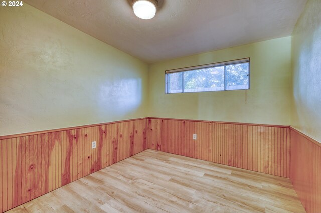 spare room with wood finished floors, wooden walls, and wainscoting