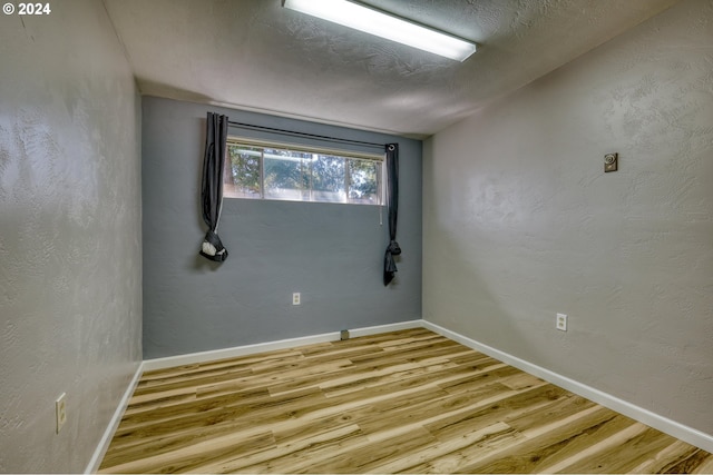 spare room with baseboards, wood finished floors, and a textured wall