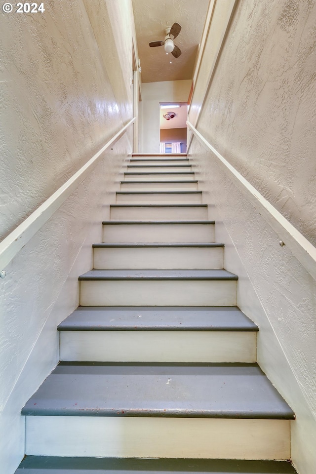stairs featuring a textured wall and a ceiling fan