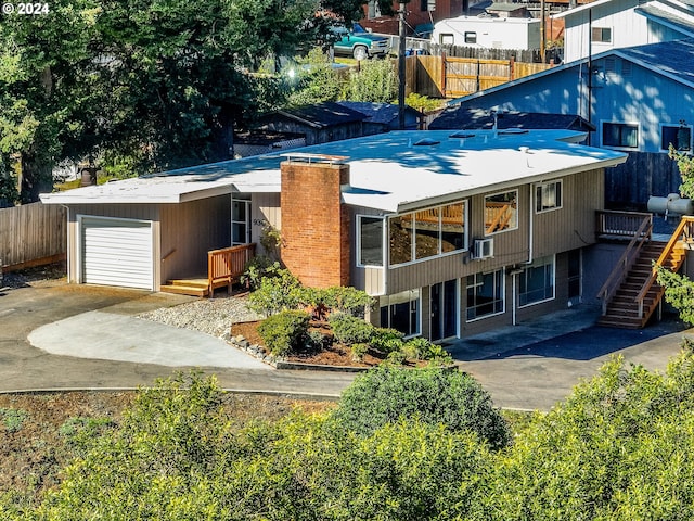 back of property with stairway, concrete driveway, a chimney, an attached garage, and fence