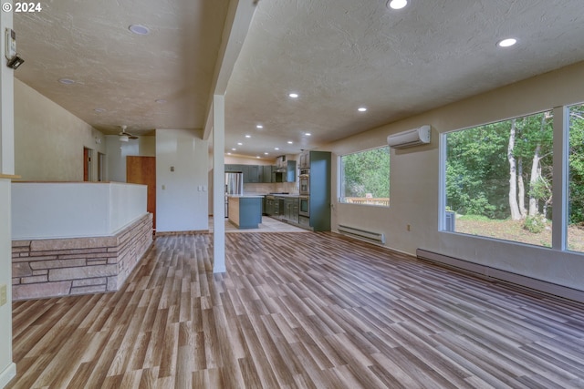 unfurnished living room featuring a baseboard heating unit, light hardwood / wood-style floors, a textured ceiling, and a wall mounted air conditioner