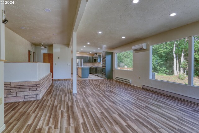 unfurnished living room with a wall mounted air conditioner, a textured ceiling, light wood-style floors, and baseboard heating