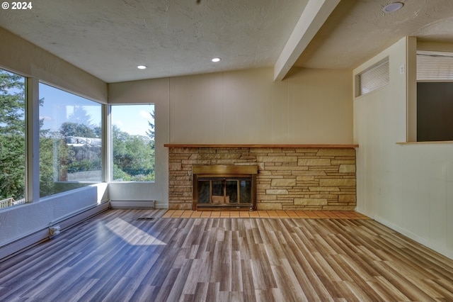 unfurnished living room featuring a textured ceiling, vaulted ceiling with beams, a stone fireplace, and hardwood / wood-style floors