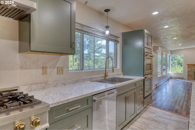 kitchen with stainless steel appliances, light wood-type flooring, decorative light fixtures, sink, and extractor fan