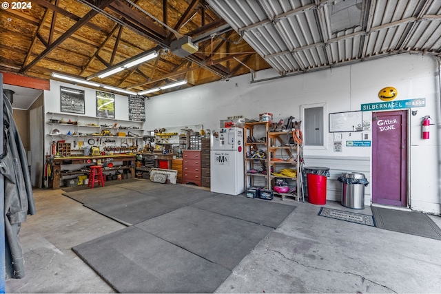 garage featuring a workshop area, electric panel, and white fridge