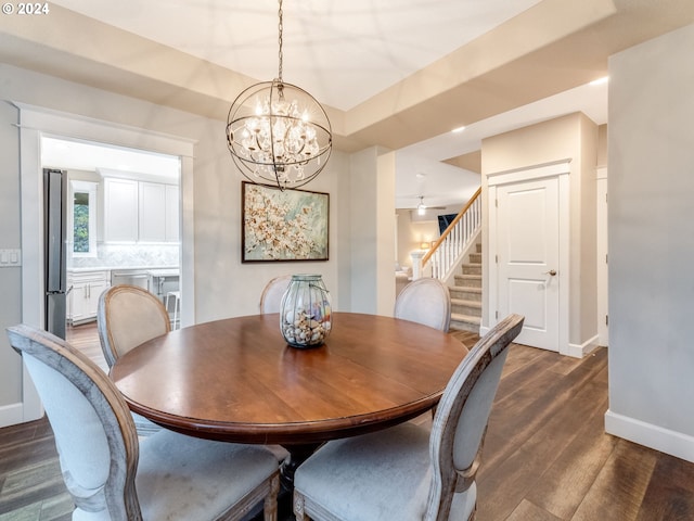 dining room with ceiling fan with notable chandelier and dark wood-type flooring