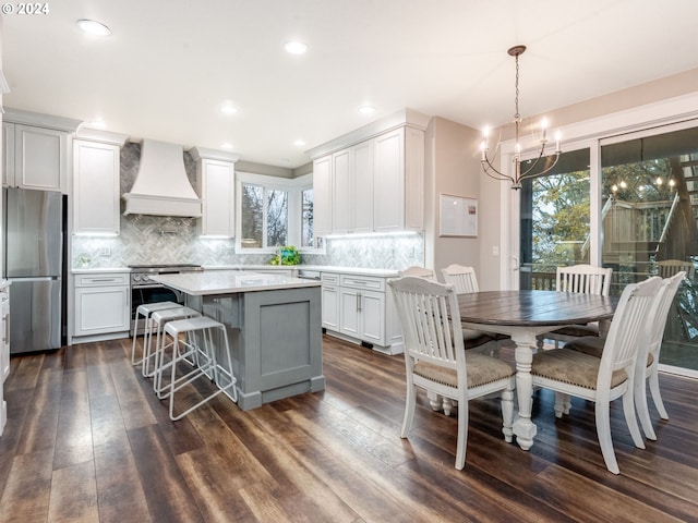 kitchen with appliances with stainless steel finishes, custom range hood, dark wood-type flooring, pendant lighting, and a center island