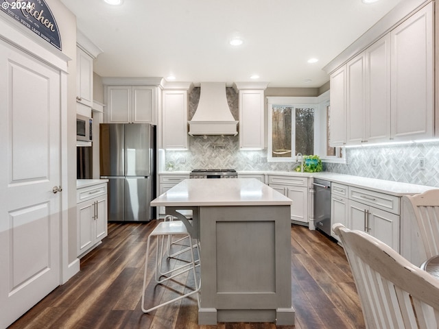 kitchen featuring premium range hood, a breakfast bar, stainless steel appliances, dark wood-type flooring, and a kitchen island