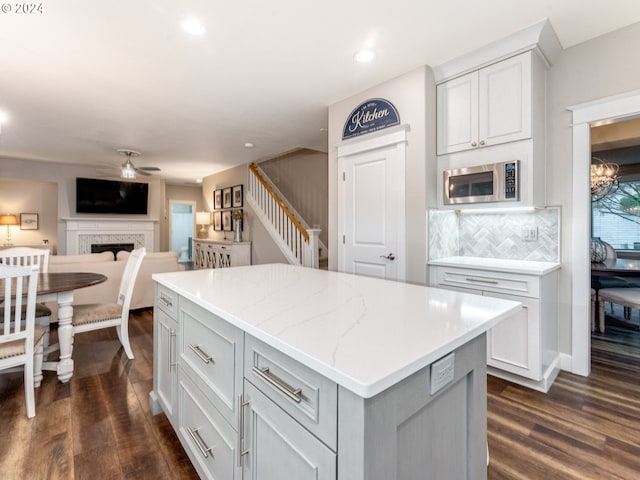 kitchen with stainless steel microwave, dark wood-type flooring, ceiling fan with notable chandelier, decorative backsplash, and a kitchen island