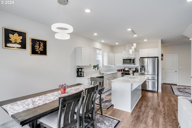 kitchen featuring stainless steel appliances, sink, decorative light fixtures, a kitchen island, and hardwood / wood-style flooring