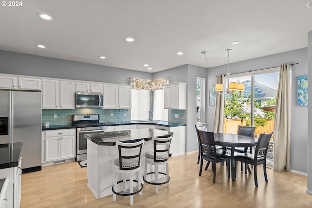 kitchen with stainless steel appliances, white cabinets, light hardwood / wood-style floors, and hanging light fixtures