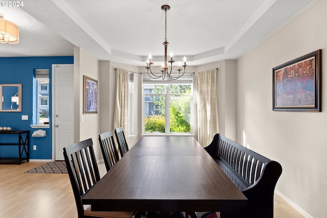 dining space featuring a tray ceiling, an inviting chandelier, and light hardwood / wood-style flooring