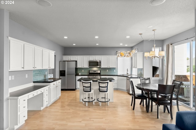 kitchen featuring white cabinetry, hanging light fixtures, a kitchen island, light hardwood / wood-style flooring, and appliances with stainless steel finishes