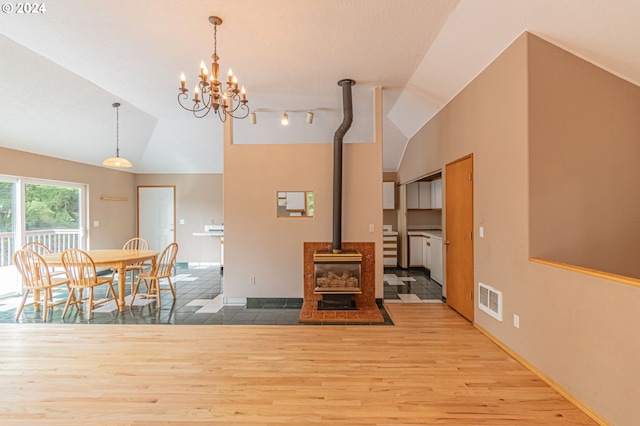 dining room featuring wood-type flooring, a chandelier, vaulted ceiling, and a wood stove