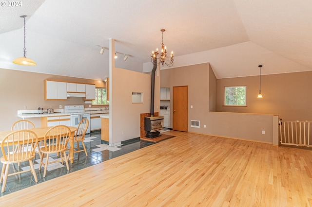 dining area with a chandelier, light hardwood / wood-style floors, washer / dryer, a wood stove, and lofted ceiling