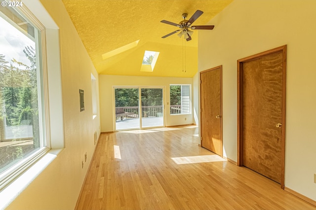 unfurnished room with ceiling fan, a skylight, a textured ceiling, high vaulted ceiling, and light hardwood / wood-style floors