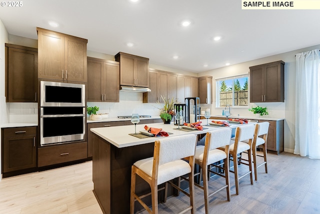 kitchen featuring light hardwood / wood-style floors, stainless steel gas cooktop, a kitchen island with sink, and a breakfast bar area