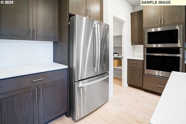 kitchen featuring tasteful backsplash, dark brown cabinets, stainless steel appliances, and light wood-type flooring